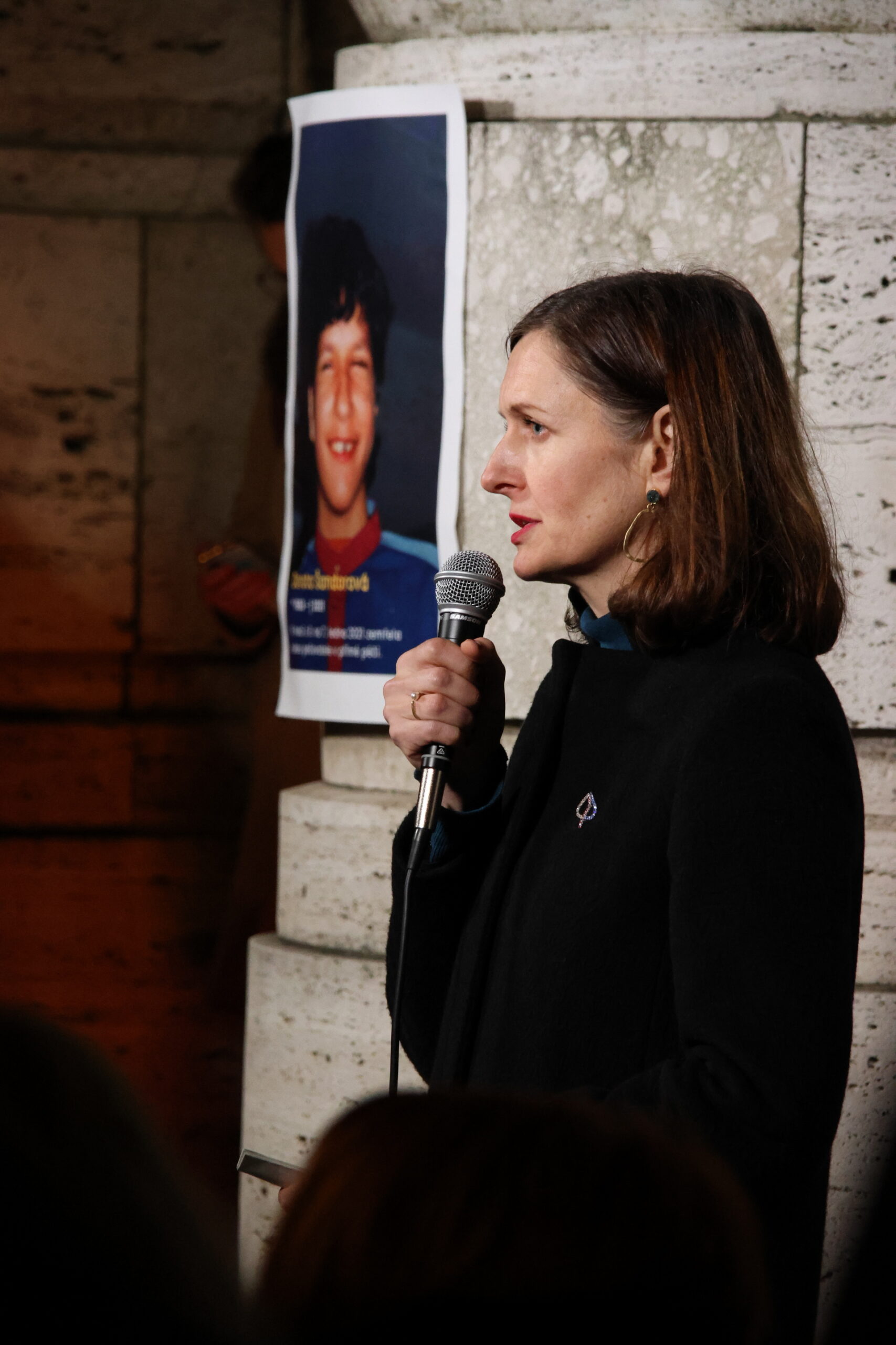 zmocněnkyně za lidská práva Klára Laurenčíková s mikrofonem v ruce, v pozadí plakát s Dorou Šandorovou