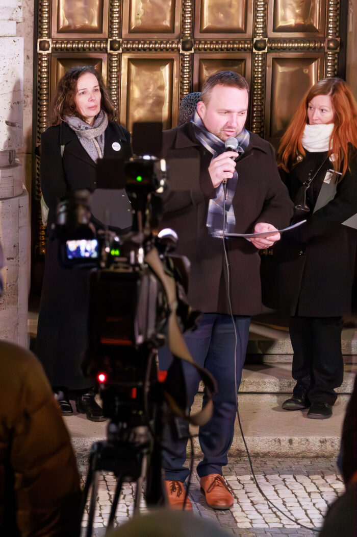 Ministr Marian Jurečka stojí před budovou MPSV s mikrofonem. V ruce má desky s Výzvou Roku důstojnosti. V pozadí stojí dvě ženy.